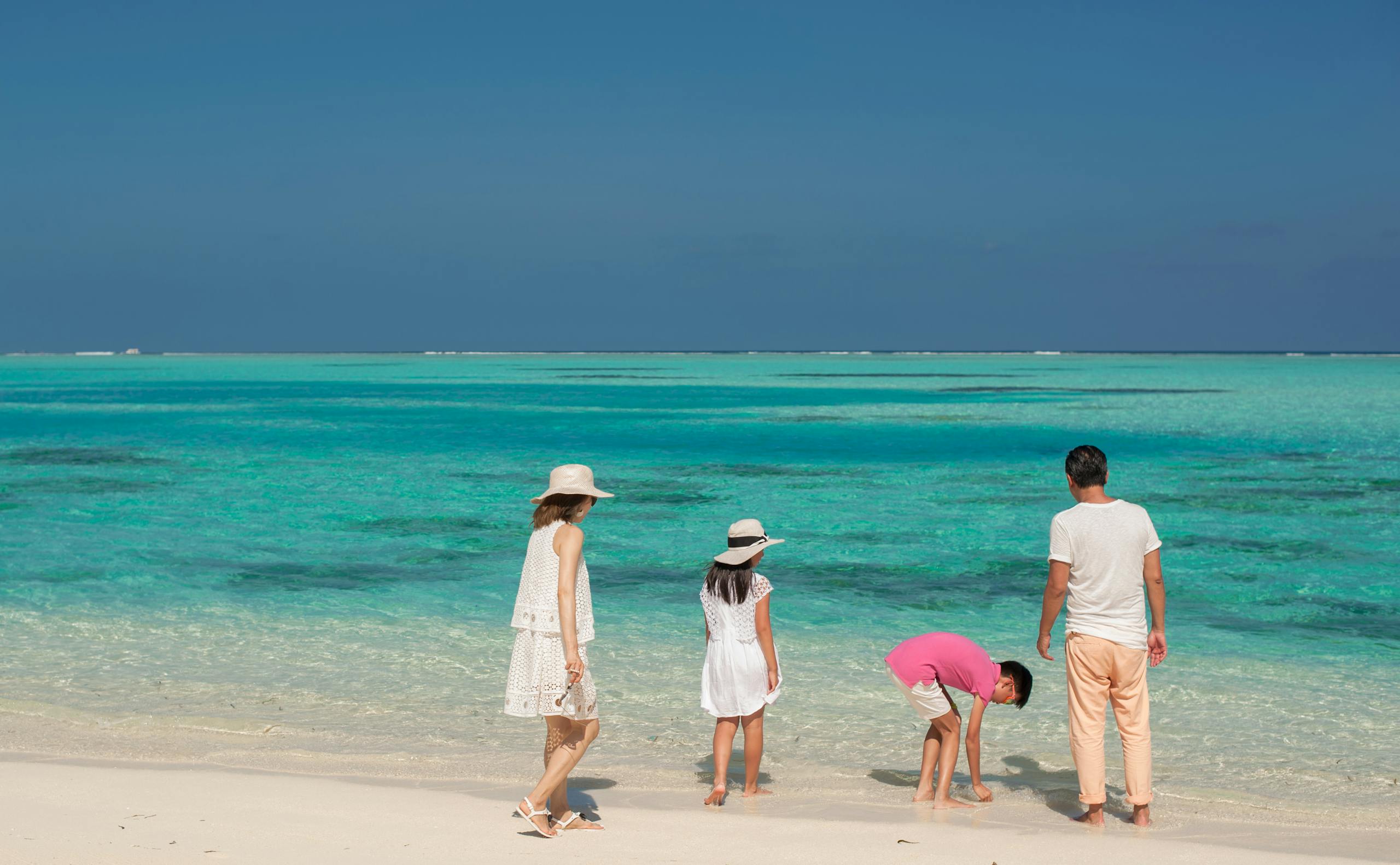 A family of four enjoying a relaxing day on a pristine sandy beach with turquoise ocean waves.