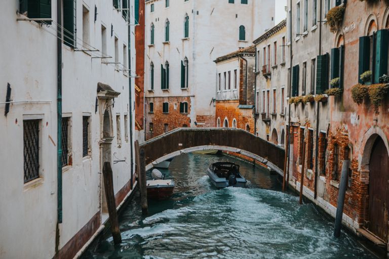 Charming Venetian canal with arched bridge and boats, showcasing classic Italian architecture.
