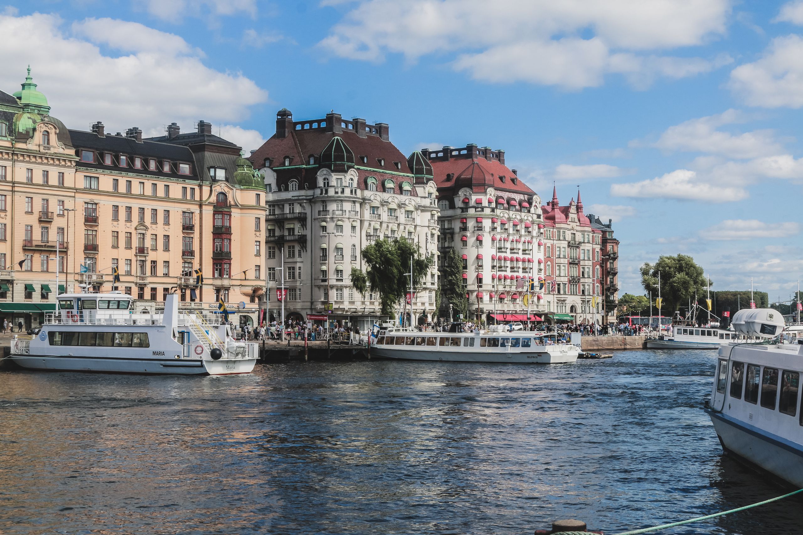 Charming view of Stockholm's historic waterfront with iconic architecture and boats under a clear sky.